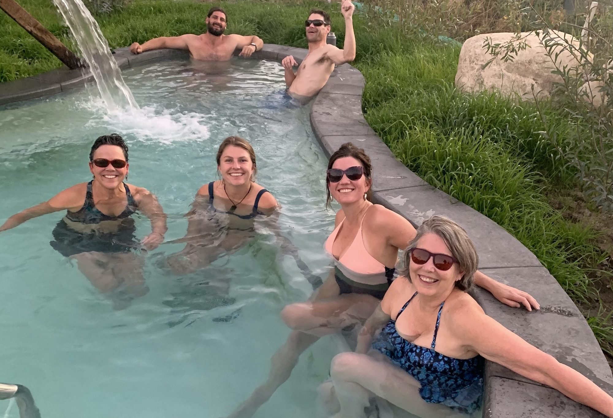 Guests relax in a hot springs pool next to grass.