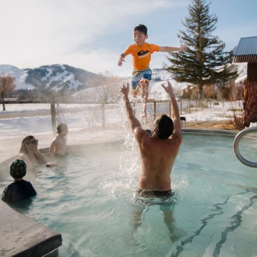 A father throws his son into the air while playing in a hot spring pool on a sunny winter day.