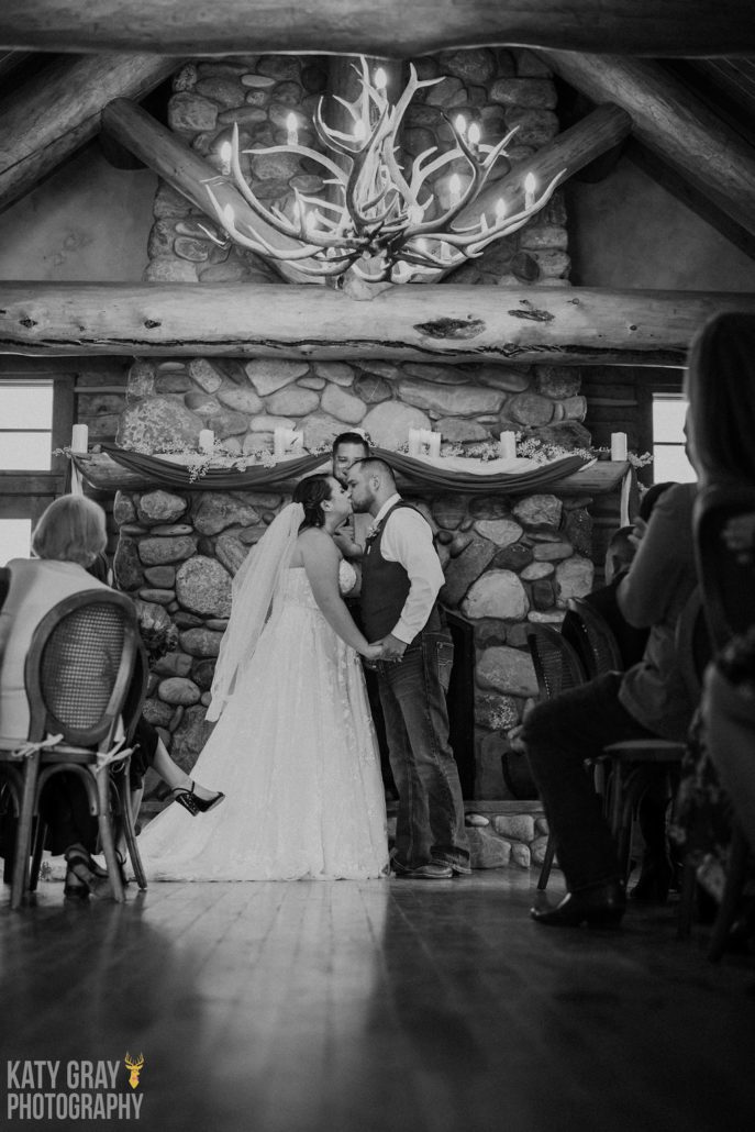 A bride and groom kiss under the alter at an indoor wedding at Astoria Hot Springs.