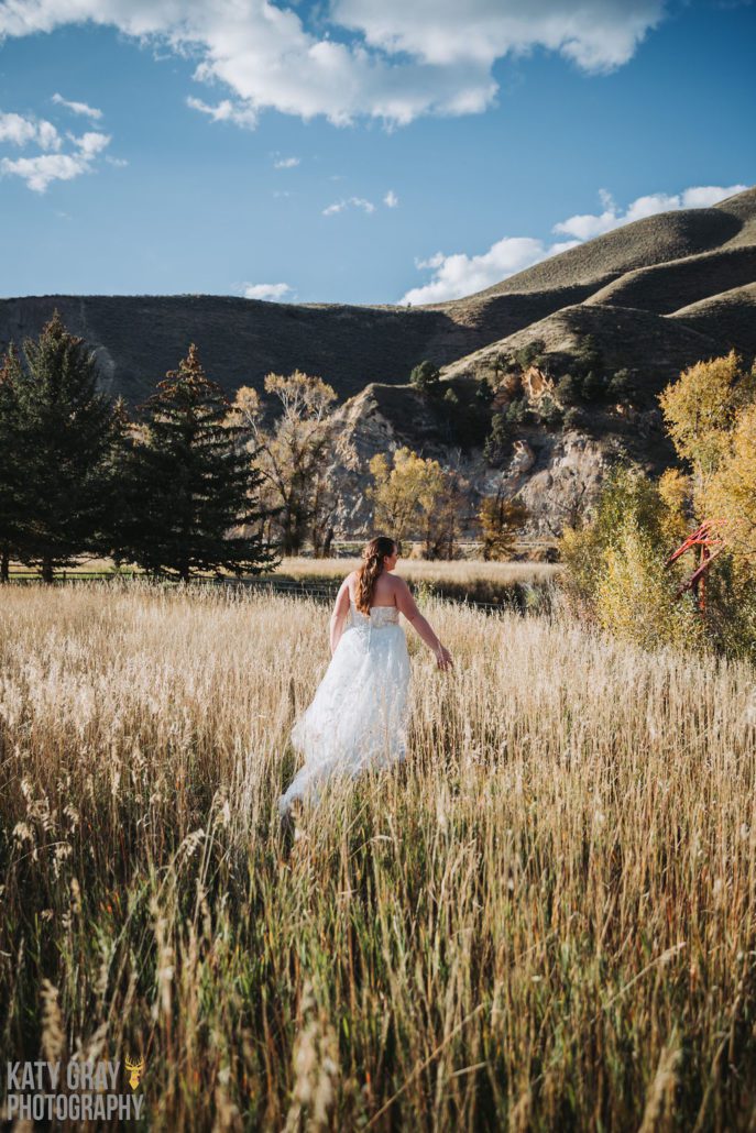 A bride walks through tall grass on a sunny day at Astoria Hot Springs.
