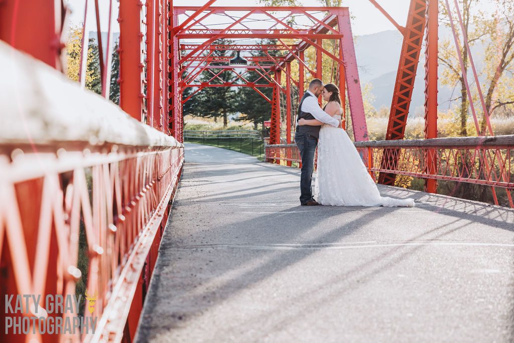 A bride and groom hug on a red bridge.