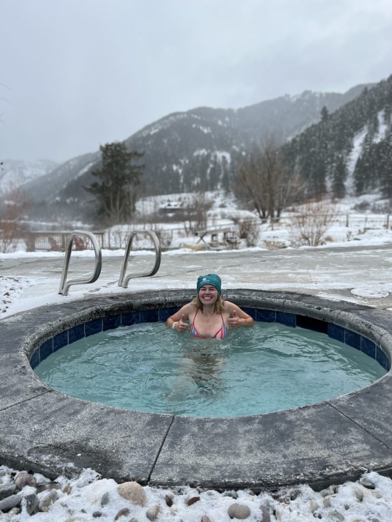 A girl wearing a blue hat dips in a cold plunge pool on a snowy winter day.