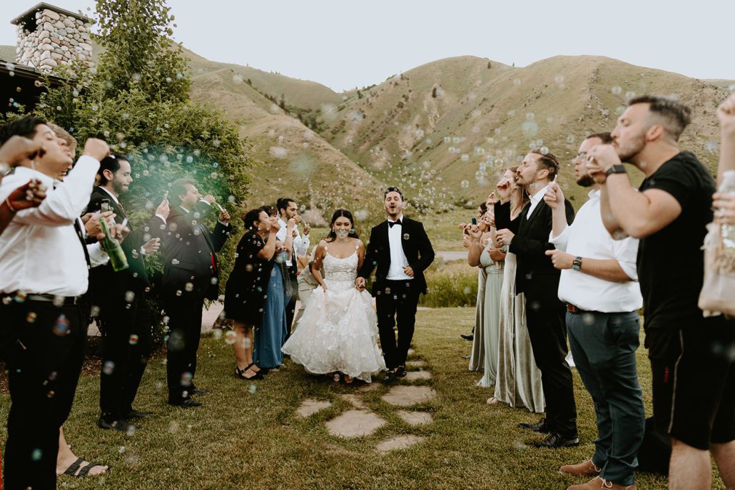 A bride and groom walk down an aisle of guests blowing bubbles outside at Astoria Hot Springs.