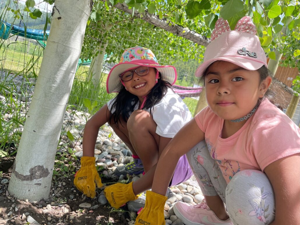 Two young girls wearing work gloves help pull weeds.